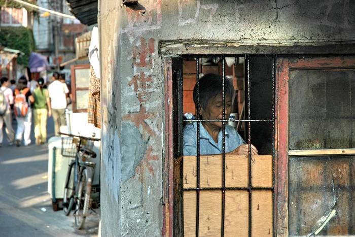 Ein Fenster mit einem Gitter davor, dahinter eine ältere Frau.