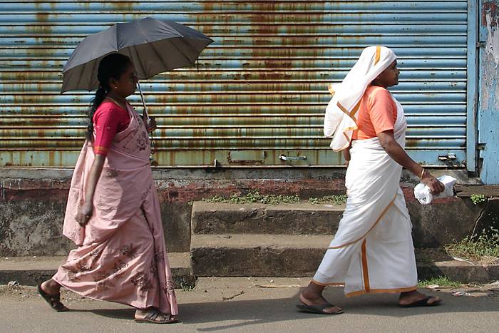 Zwei Frauen mit Regenschirmen bei Sonnenschein.