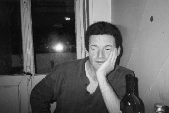 Schwarzweiss-Foto: Ein Mann sitzt mit einer Flasche Wein an einem Tisch, im Hintergrund ein Fenster.