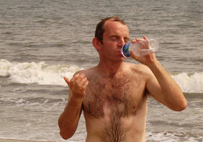Ein Mann trinkt Wasser aus einer Flasche, am Meer.