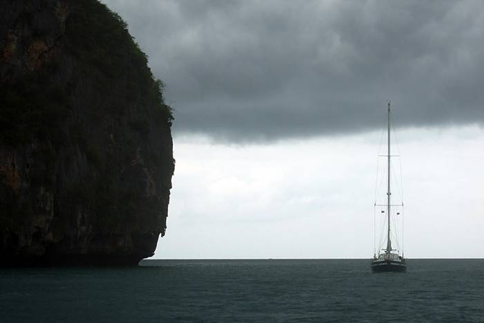 Ein Segelschiff neben einem runden, dunklen Felsen.